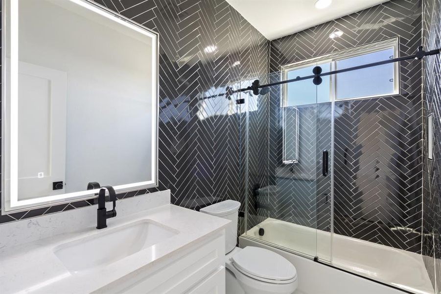 Full bathroom with shower / bath combination with glass door, vanity, toilet, and tile walls