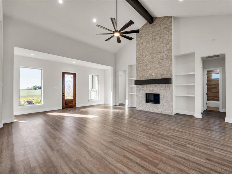 Unfurnished living room with hardwood / wood-style floors, beam ceiling, ceiling fan, high vaulted ceiling, and a stone fireplace