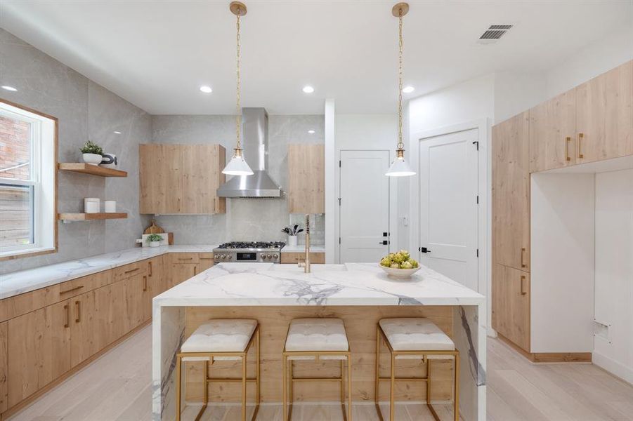 This kitchen features waterfall quartz counters, white oak cabinetry, brass fixtures and ceiling height book matched backsplash.