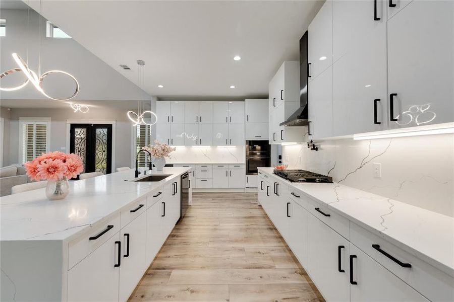 Kitchen featuring a large island with sink, white cabinetry, light wood-type flooring, decorative light fixtures, and sink