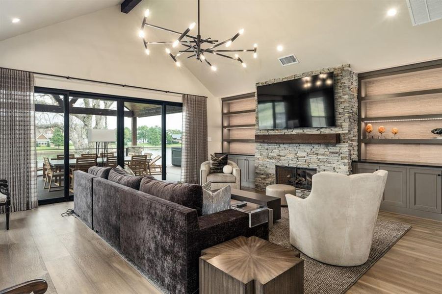 Living room with a fireplace, high vaulted ceiling, a notable chandelier, and light hardwood / wood-style floors