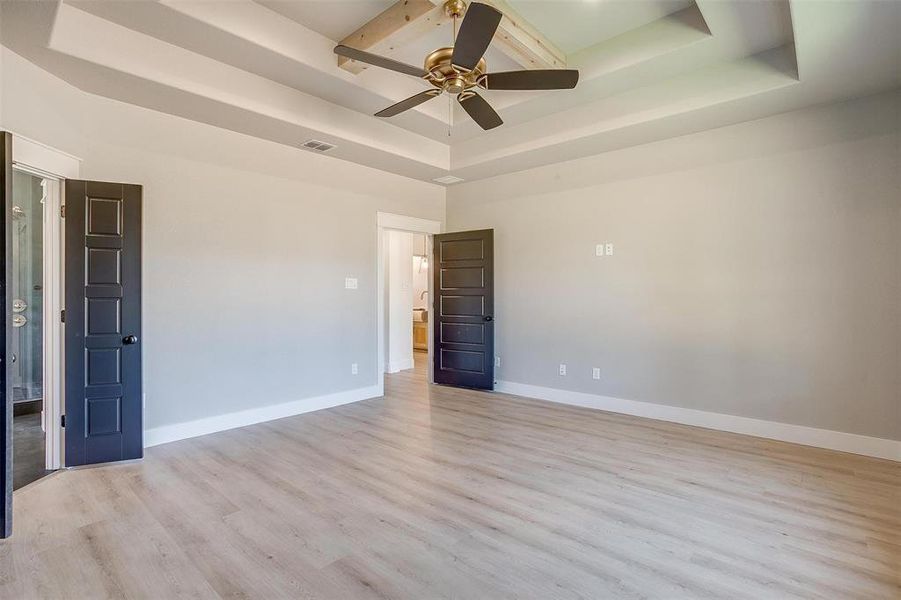 Empty room with ceiling fan, a tray ceiling, and light hardwood / wood-style floors