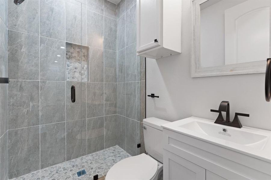 Bathroom featuring a shower with door, toilet, and vanity