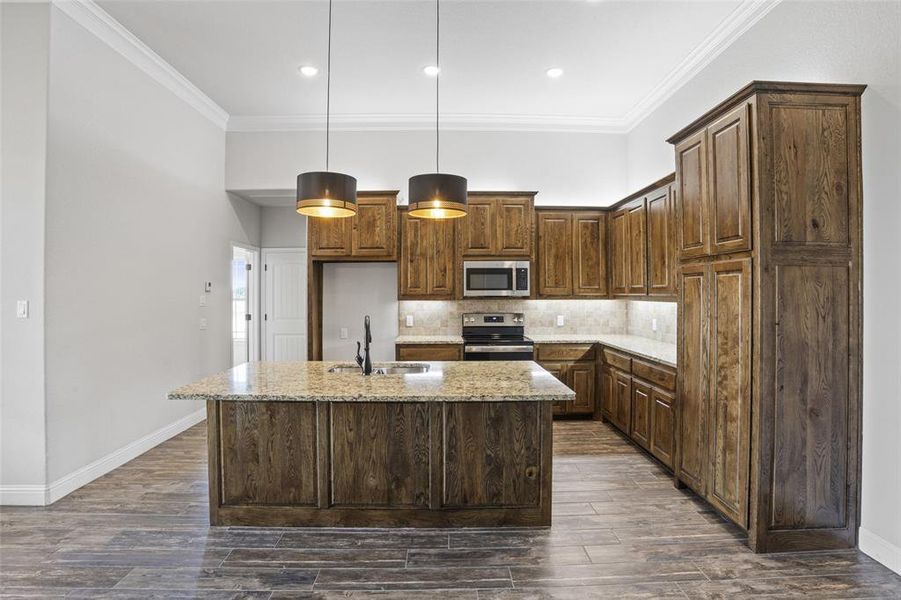 Kitchen featuring appliances with stainless steel finishes, tasteful backsplash, dark hardwood / wood-style floors, light stone countertops, and an island with sink