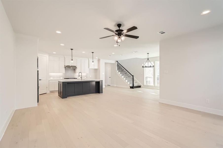 Unfurnished living room with sink, light wood-type flooring, and ceiling fan with notable chandelier