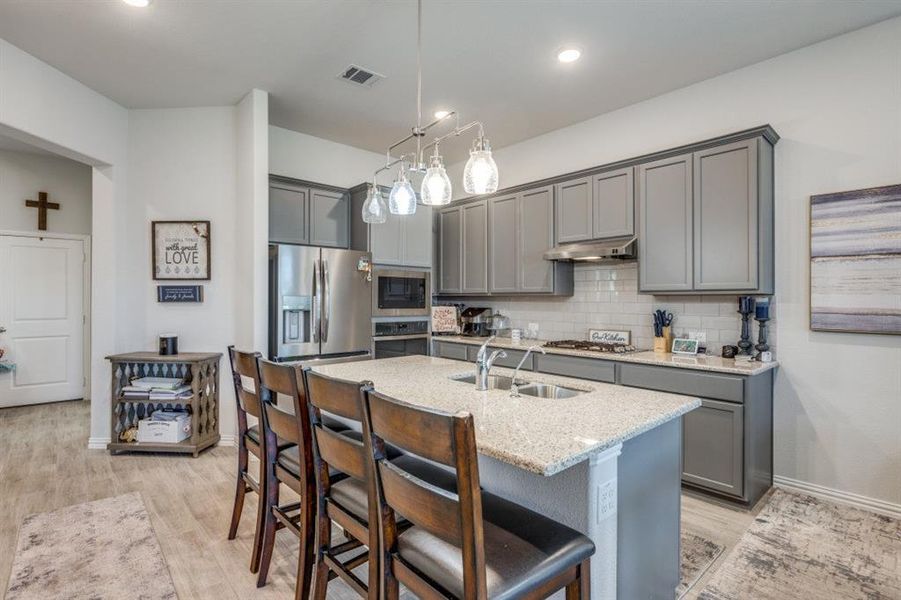 Kitchen featuring light stone counters, gray cabinetry, decorative light fixtures, appliances with stainless steel finishes, and light wood-type flooring