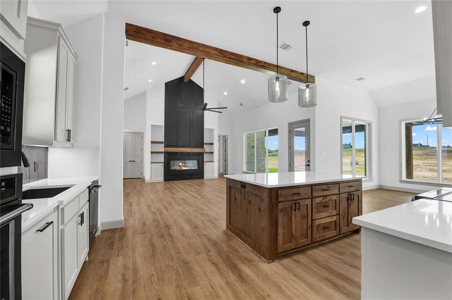 Kitchen with light wood-type flooring, white cabinetry, a center island, and beamed ceiling