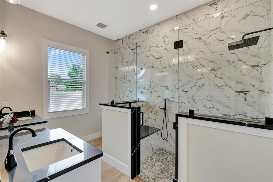 Primary bathroom with beautiful floor-to-ceiling tile work and spacious shower with bench including hand-held shower wand, his/hers sinks and vanity counter in between
