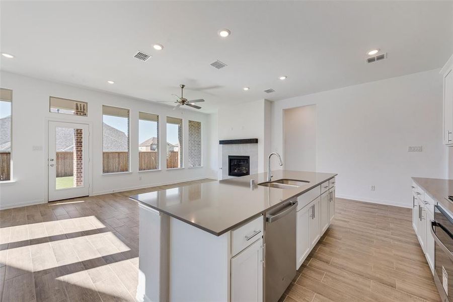 Kitchen with sink, light wood-type flooring, dishwasher, an island with sink, and white cabinetry