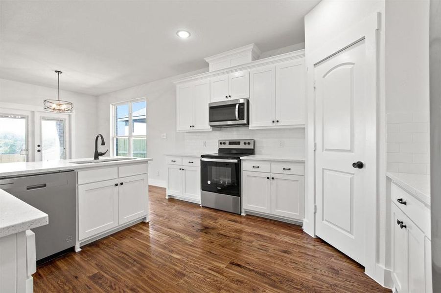 Kitchen featuring sink, white cabinetry, hanging light fixtures, stainless steel appliances, and dark hardwood / wood-style flooring