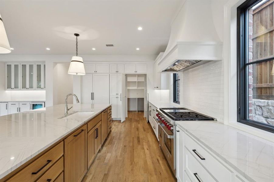 Kitchen with light stone counters, sink, white cabinetry, custom range hood, and double oven range