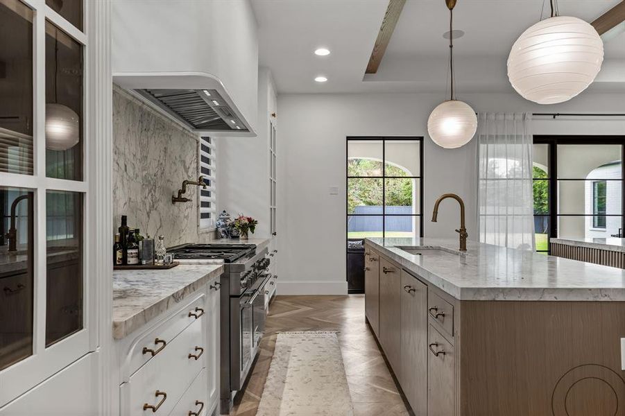 Kitchen featuring decorative light fixtures, a center island with sink, stainless steel stove, and sink