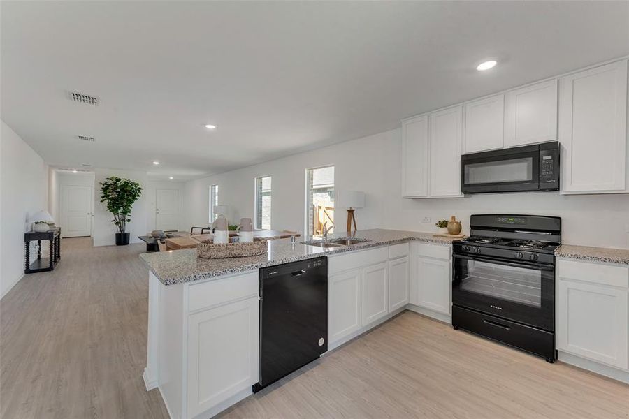 Kitchen featuring black appliances, kitchen peninsula, light wood-type flooring, and white cabinetry