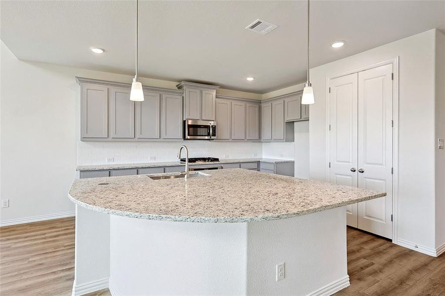 Kitchen featuring light stone countertops, sink, light wood-type flooring, and a center island with sink