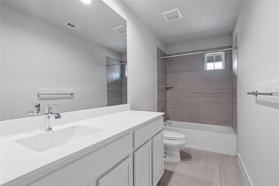 Secondary bathroom features light countertops and cabinets, neutral paint, shower/tub combo with tile surround, large mirror, tile floors, sleek fixtures and modern finishes, plenty of space to accommodate any visiting family or guests.