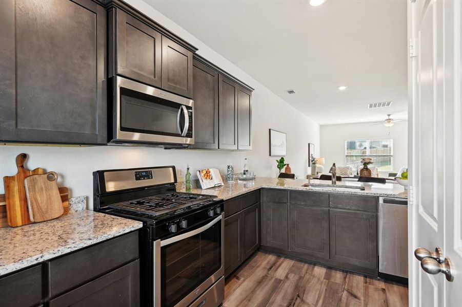 Kitchen featuring light wood-type flooring, light stone counters, sink, appliances with stainless steel finishes, and dark brown cabinetry