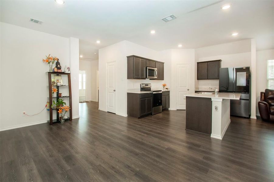 Kitchen featuring dark wood-type flooring, stainless steel appliances, a kitchen island with sink, and dark brown cabinets
