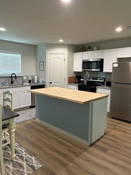 Kitchen featuring appliances with stainless steel finishes, a center island, white cabinets, and hardwood / wood-style floors