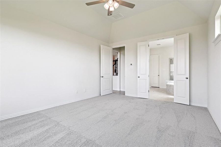 Unfurnished bedroom featuring connected bathroom, lofted ceiling, ceiling fan, and light colored carpet