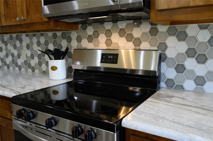 Kitchen featuring light stone counters, tasteful backsplash, and appliances with stainless steel finishes