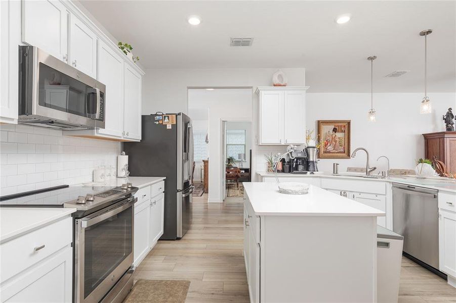 Kitchen with light hardwood / wood-style flooring, white cabinets, and appliances with stainless steel finishes