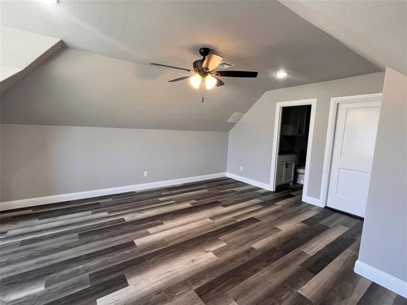 Bonus room with ceiling fan, dark wood-type flooring, vaulted ceiling, and a textured ceiling