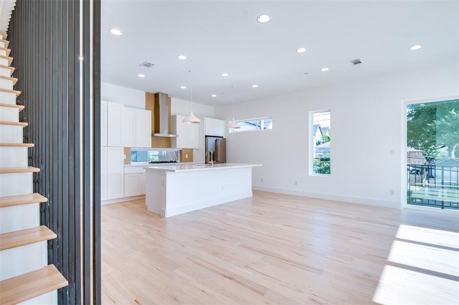 Kitchen with high end fridge, hanging light fixtures, white cabinetry, wall chimney exhaust hood, and light hardwood / wood-style flooring