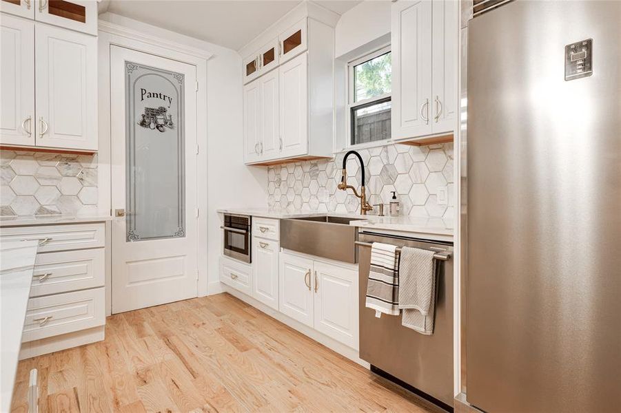 Kitchen featuring white cabinets, backsplash, light wood-type flooring, appliances with stainless steel finishes, and sink