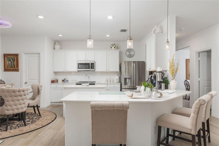 Kitchen featuring white cabinets, hanging light fixtures, stainless steel appliances, light wood-type flooring, and decorative backsplash