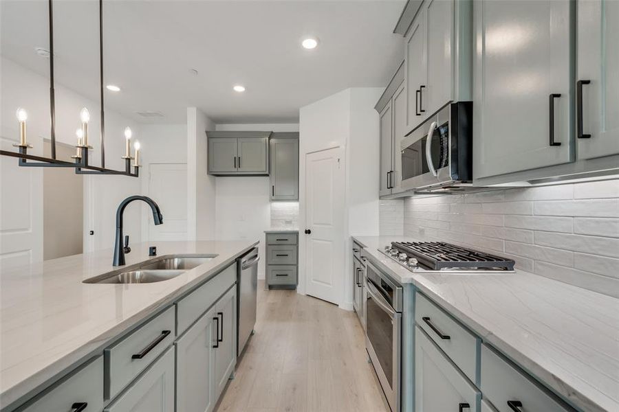 Kitchen featuring tasteful backsplash, light stone countertops, appliances with stainless steel finishes, and light wood-type flooring