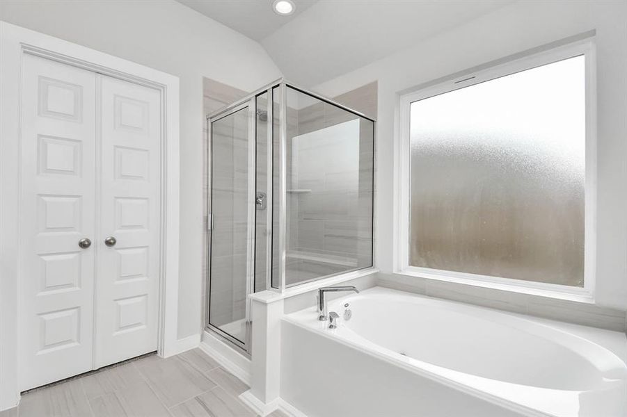 Delight in a spacious walk-in shower enveloped in stylish tile surround, unwind in a separate garden tub adorned with custom detailing. Sample photo of completed home with similar plan. Actual color and selections may vary.