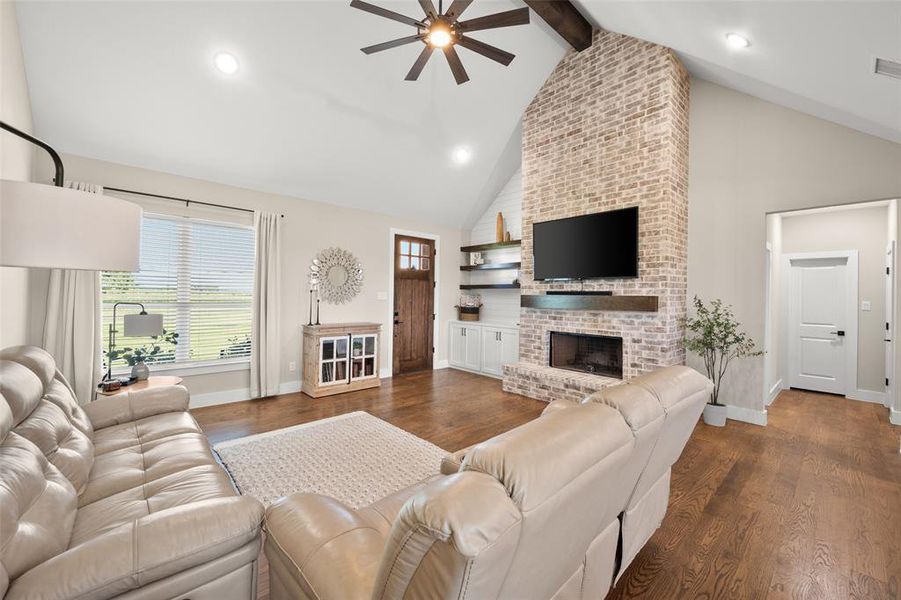 Living room featuring high vaulted ceiling,  hardwood flooring, ceiling fan, and a fireplace