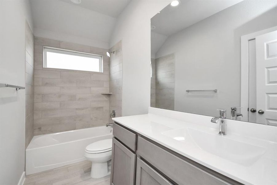 Secondary bath features tile flooring, bath/shower combo with tile surround, light stained wood cabinets, beautiful light countertop. Sample photo of completed home with similar plan. Actual color and selections may vary.