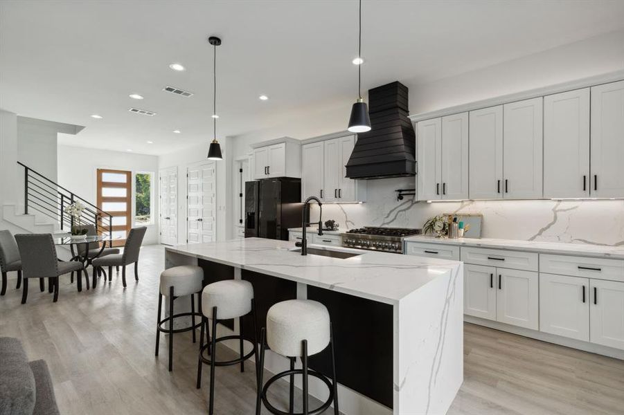 Kitchen featuring black fridge, sink, an island with sink, and white cabinets