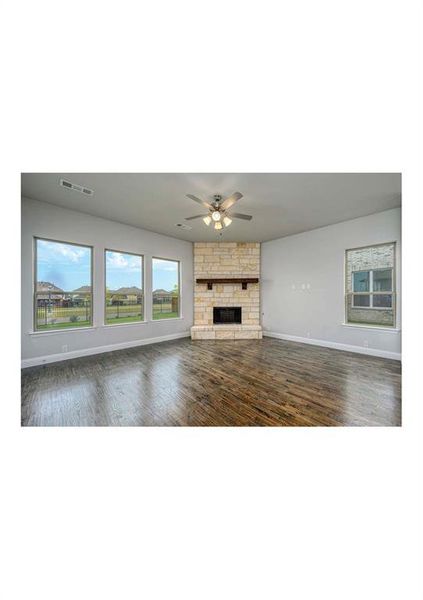 Unfurnished living room with dark hardwood / wood-style floors, a stone fireplace, and ceiling fan