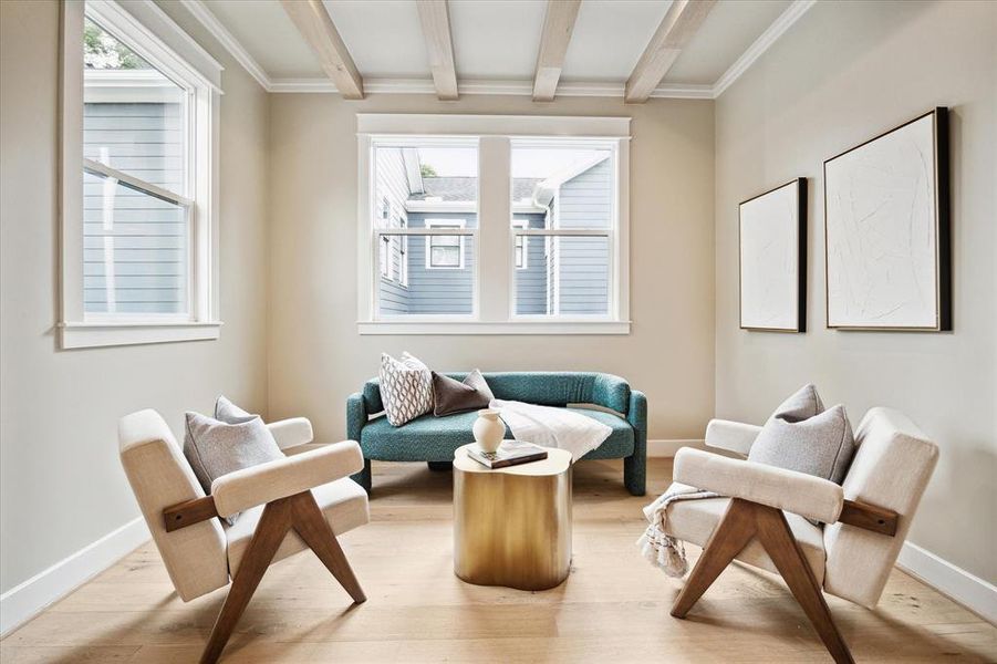 The sitting area is an inviting and cozy space. Large windows flood the area with natural light and the ceiling features wood beams that add texture. The overall design blends elegance with comfort, creating a serene retreat within the primary bedroom.