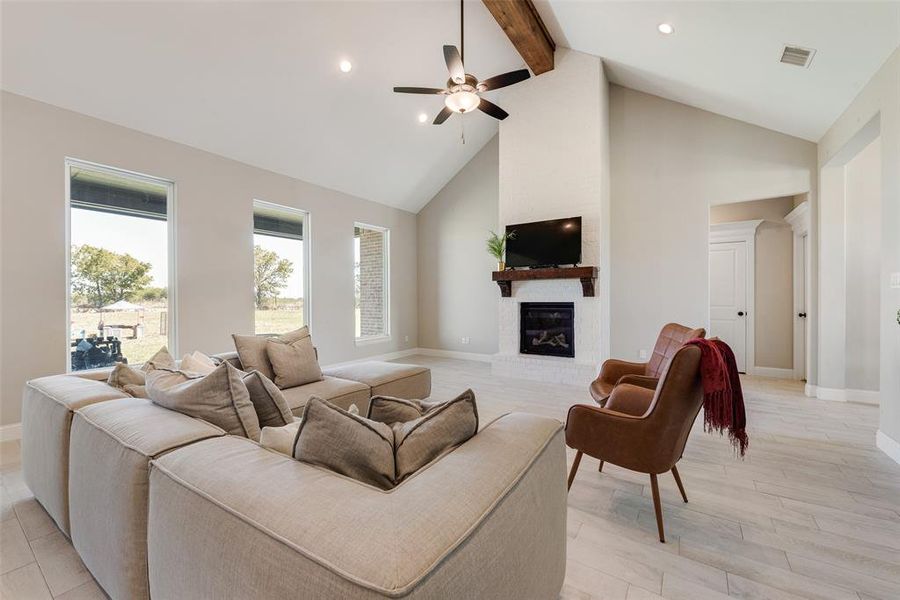 Living room with beam ceiling, light hardwood / wood-style flooring, a brick fireplace, high vaulted ceiling, and ceiling fan