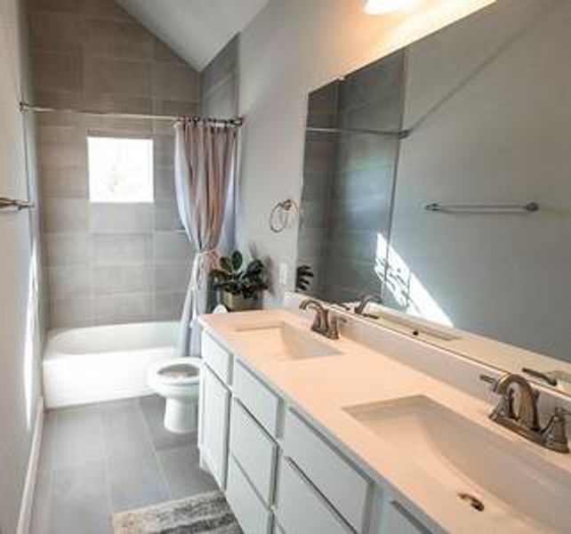 Full bathroom with vanity, lofted ceiling, toilet, tile patterned flooring, and shower / tub combo with curtain