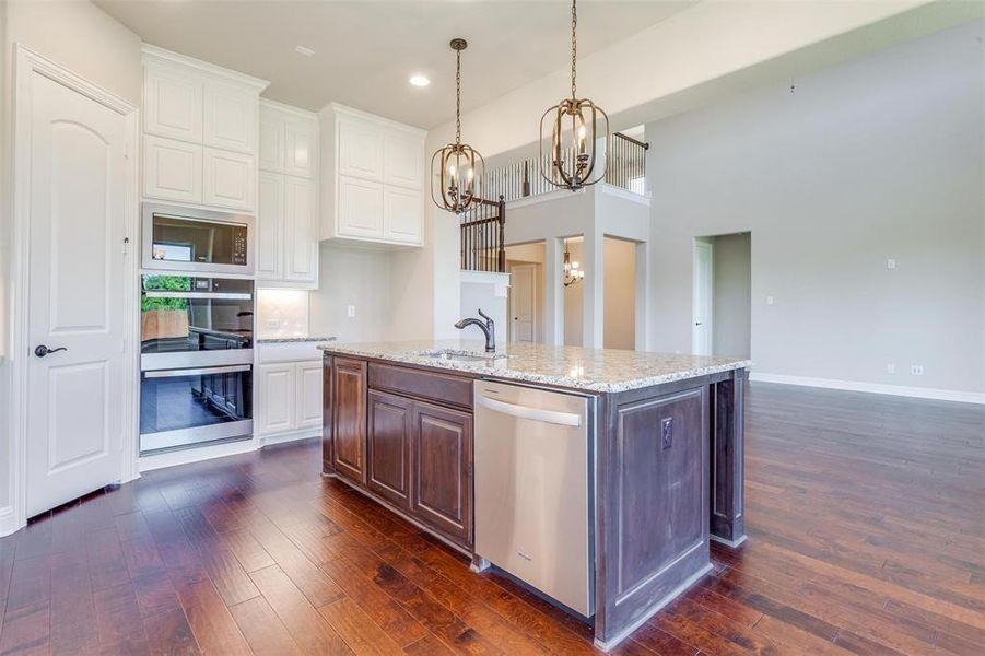 Kitchen with dishwasher, dark wood-type flooring, white cabinetry, and an island with sink