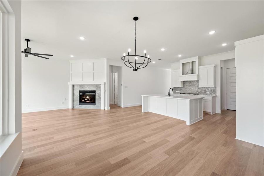 Kitchen featuring white cabinetry, light hardwood / wood-style flooring, tasteful backsplash, ceiling fan with notable chandelier, and an island with sink