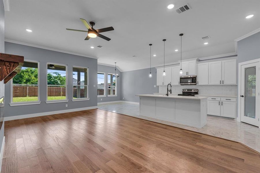 Kitchen featuring a center island with sink, light wood-type flooring, pendant lighting, white cabinets, and appliances with stainless steel finishes