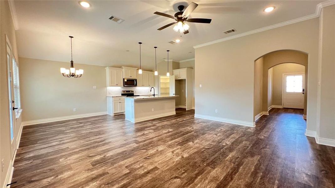 Unfurnished living room featuring ceiling fan with notable chandelier, ornamental molding, sink, and dark wood-type flooring