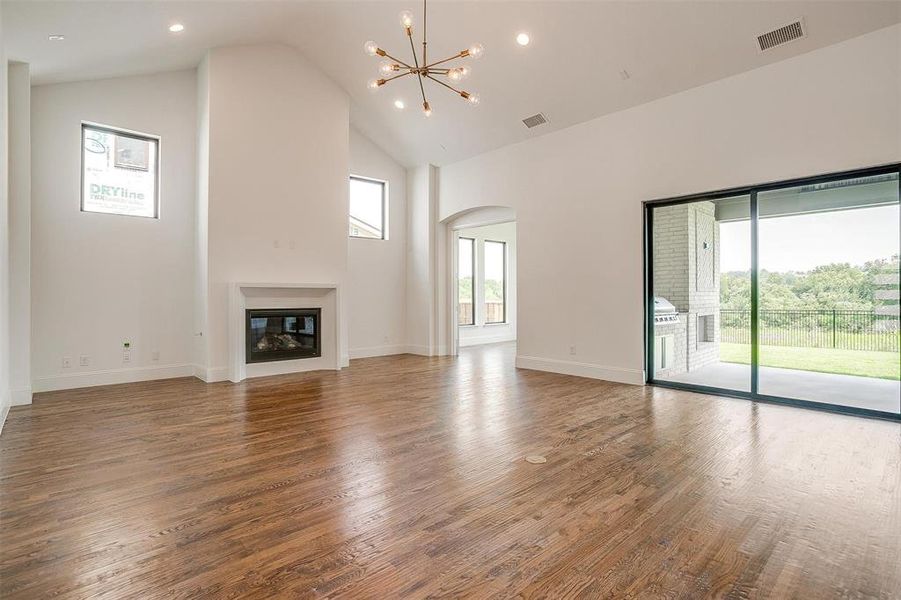 Unfurnished living room featuring high vaulted ceiling, hardwood / wood-style floors, and a notable chandelier