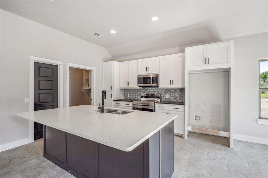 Kitchen featuring appliances with stainless steel finishes, sink, an island with sink, backsplash, and white cabinets