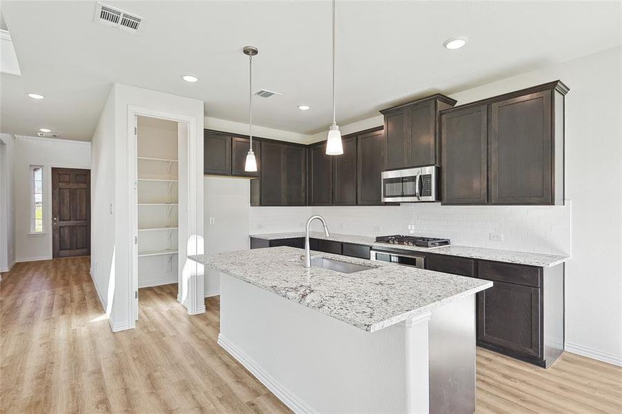 Kitchen with light hardwood / wood-style floors, hanging light fixtures, stainless steel appliances, light stone counters, and sink