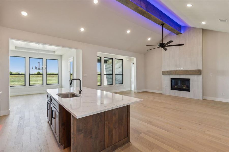 Kitchen with lofted ceiling with beams, light stone countertops, light wood-type flooring, sink, and a center island with sink