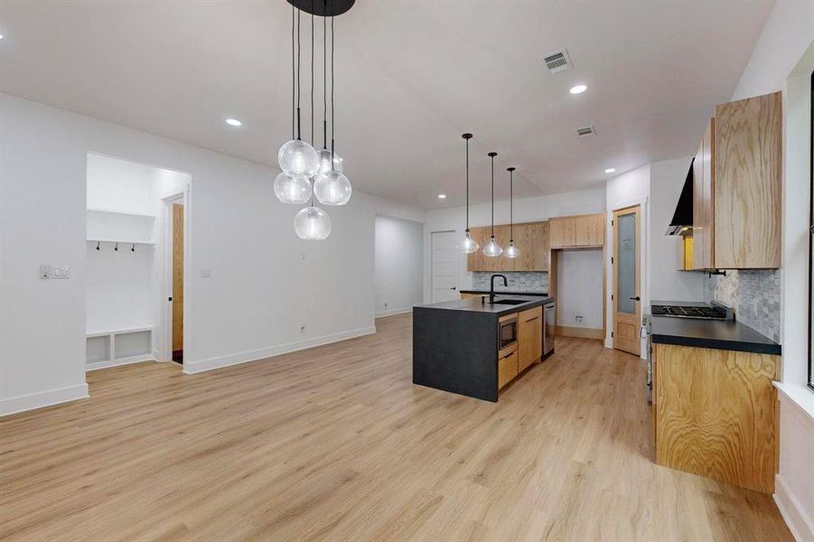 Kitchen with sink, light hardwood / wood-style floors, pendant lighting, a center island with sink, and backsplash