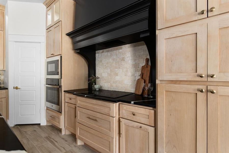 Kitchen with stainless steel appliances, light wood-type flooring, light brown cabinetry, and tasteful backsplash