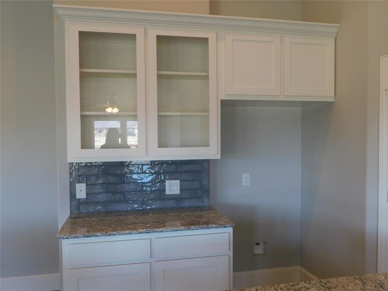 Kitchen featuring white cabinets, stone countertops, and decorative backsplash