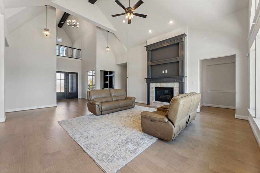 Living room featuring high vaulted ceiling, ceiling fan with notable chandelier, hardwood / wood-style flooring, and a fireplace